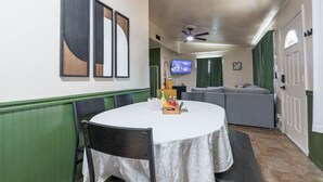 A dining area with a round table, chairs, and a television mounted on the wall. - Bison Hill Bungalow | 3 blks from OBU (Shawnee)