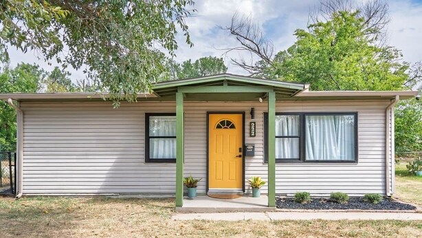 A single-story house with a yellow front door, two windows, and a small porch with potted plants. - Bison Hill Bungalow | 3 blks from OBU (Shawnee)