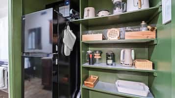 A kitchen with a black refrigerator, shelves with kitchenware, and a wooden cutting board.