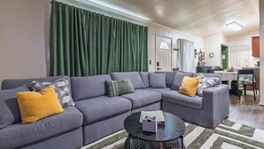 A living room with a sectional sofa, a coffee table, and a green curtain. - Bison Hill Bungalow | 3 blks from OBU (Shawnee)