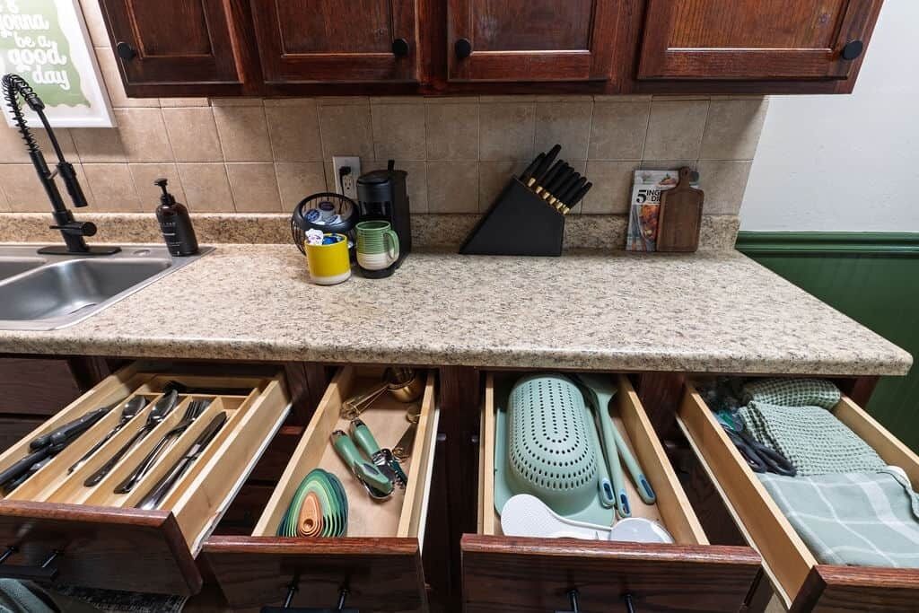 A kitchen with wooden cabinets, a granite countertop, and a drawer organizer with utensils.