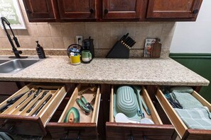A kitchen with wooden cabinets, a granite countertop, and a drawer organizer with utensils. - Bison Hill Bungalow | 3 blks from OBU (Shawnee)