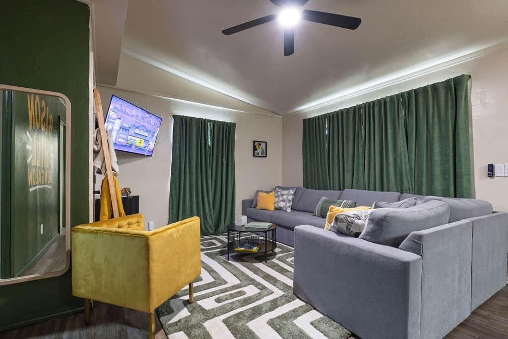A living room with a sofa, a yellow armchair, a coffee table, a ceiling fan, and a television.