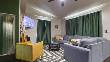 A living room with a sofa, a yellow armchair, a coffee table, a ceiling fan, and a television.