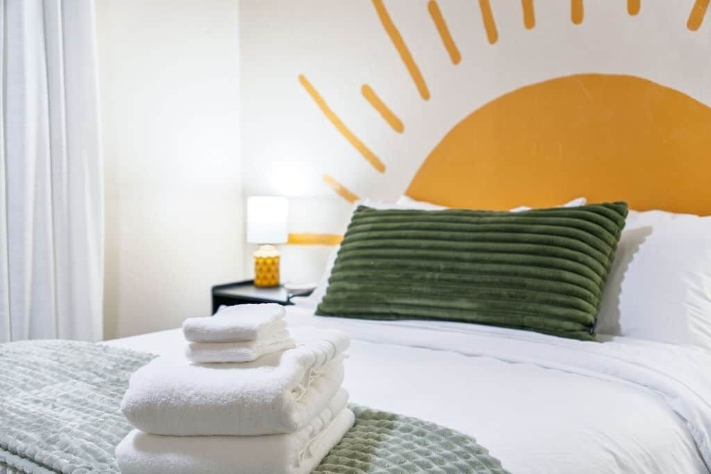 Una cama bien hecha con un cojín verde y una pila de toallas blancas.