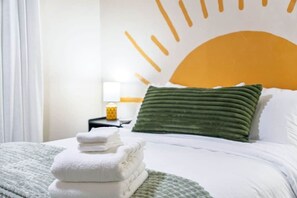 Una cama bien hecha con un cojín verde y una pila de toallas blancas.
