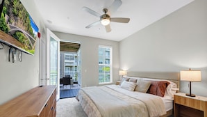 A bedroom with a bed, bedside tables, a ceiling fan, a TV mounted on the wall, and a view of the outside balcony. - Luxe•King Suite Universal/Epic•6 Min•Getaway (Orlando)