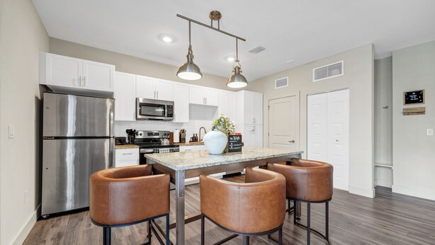 A modern kitchen with stainless steel appliances, a marble countertop, and bar stools. - Luxe•King Suite Universal/Epic•6 Min•Getaway (Orlando)