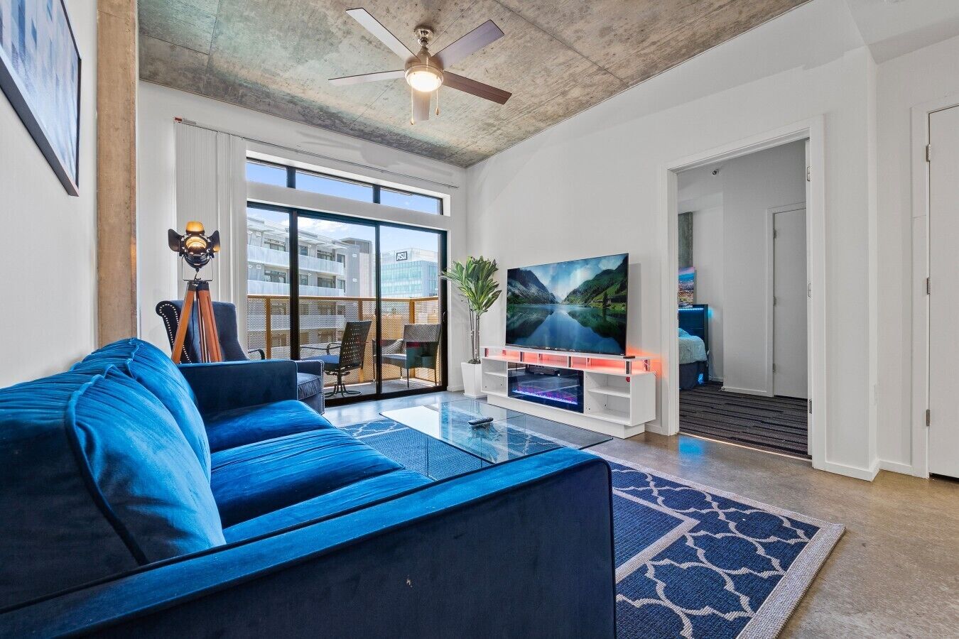 Een moderne woonkamer met een grote flatscreen televisie, een blauwe bank en een plafondventilator.
