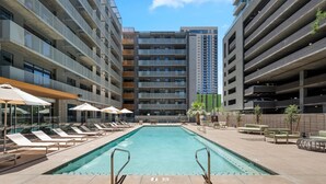 Une piscine entourée d’immeubles de grande hauteur, avec des chaises longues et des parasols.