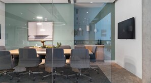 A modern meeting room with a glass partition, a wooden table, grey office chairs, and pendant lighting. - Phoenix Downtown Zen Loft (Phoenix)