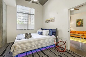 A bedroom with a bed, a window, a painting, and a sofa in the adjacent room. - Phoenix Downtown Zen Loft (Phoenix)