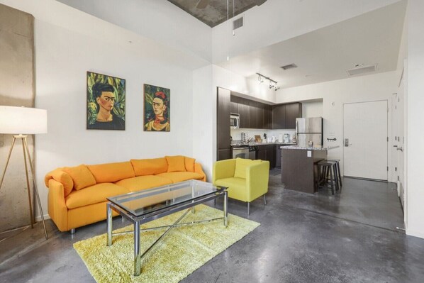 A modern living room with a sofa, a yellow armchair, and a glass coffee table. There is a kitchen in the background with a refrigerator and a microwave. - Phoenix Downtown Zen Loft (Phoenix)