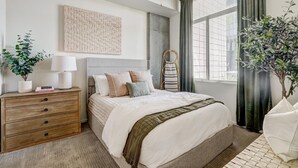 Een netjes ingerichte slaapkamer met een bed, een dressoir en potplanten.