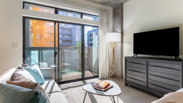 Een moderne woonkamer met een bank, een salontafel, een televisie en een balkon met uitzicht op gebouwen.