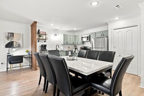Eine moderne Küche mit hellgrünen Schränken, einem Edelstahl-Kühlschrank und einem Essbereich mit einem Marmortisch und schwarzen Ledersesseln.