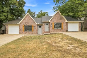 A two-story brick house with a front garage, a small front porch, and a well-maintained lawn. - Switchback Suites - Side A (Bentonville)