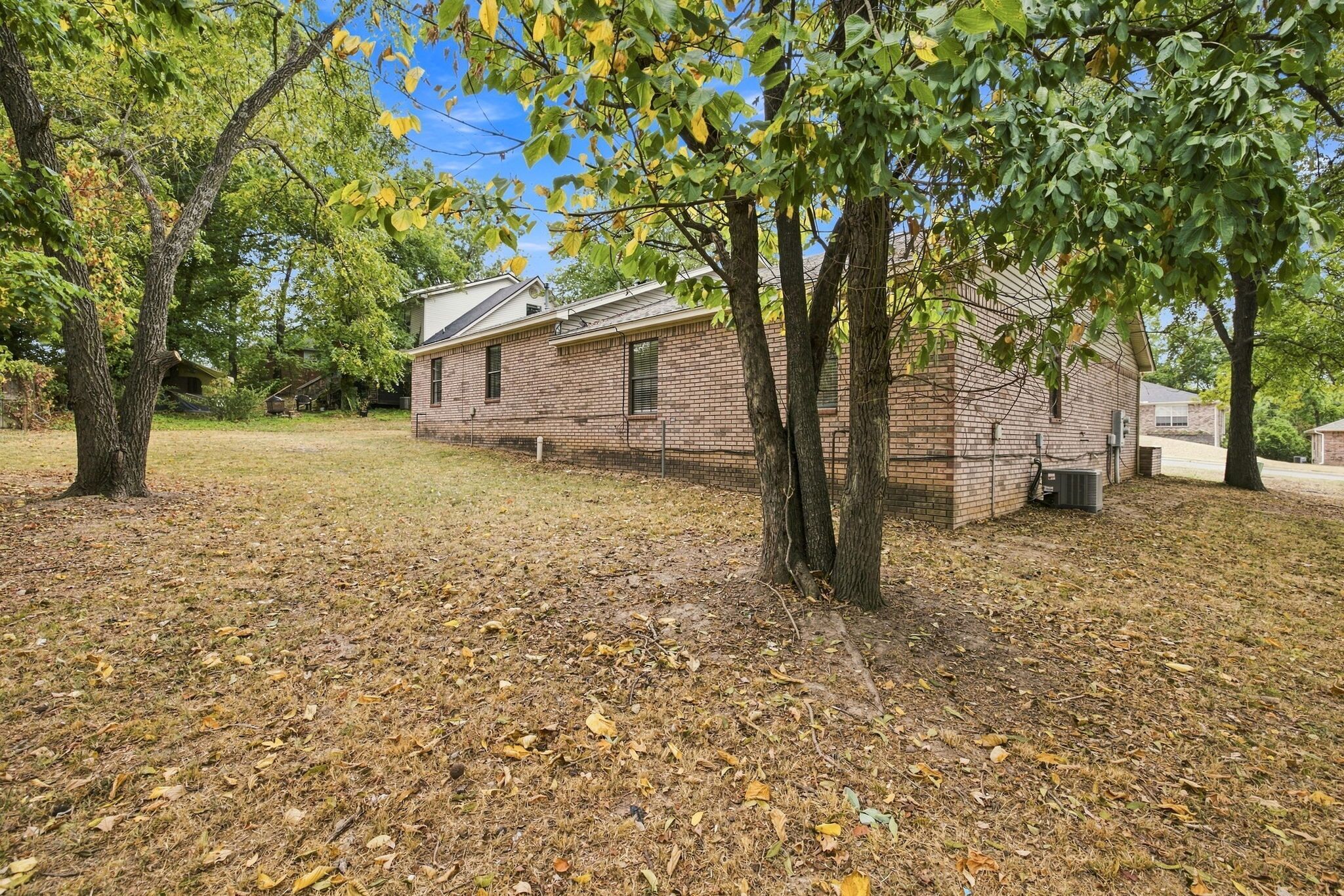 A brick building with a sloped roof, surrounded by trees and a grassy area with fallen leaves.