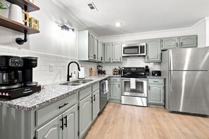 A modern kitchen with stainless steel appliances, a granite countertop, and light grey cabinetry. - Switchback Suites - Side A (Bentonville)