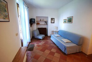 A room with a sofa, a chair, a television, a small table, and a shelf with decorative items. - Villa Opera Apartment in Arezzo (Toscana)