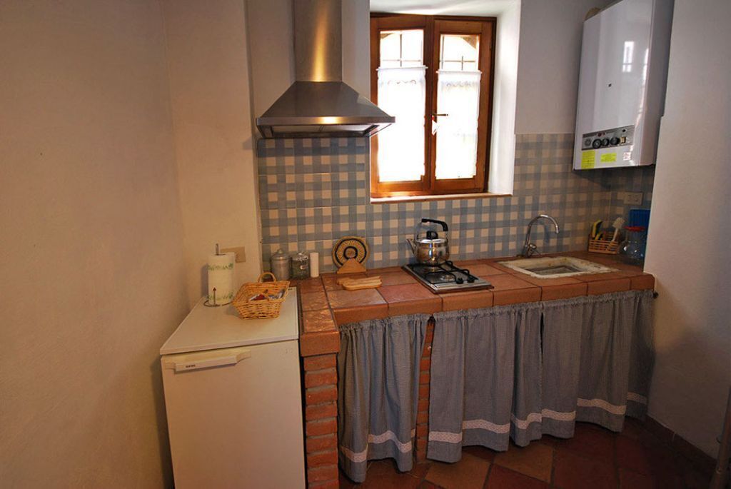Een kleine keuken met een witte koelkast, een kookplaat, een spoelbak en een raam met gordijnen.