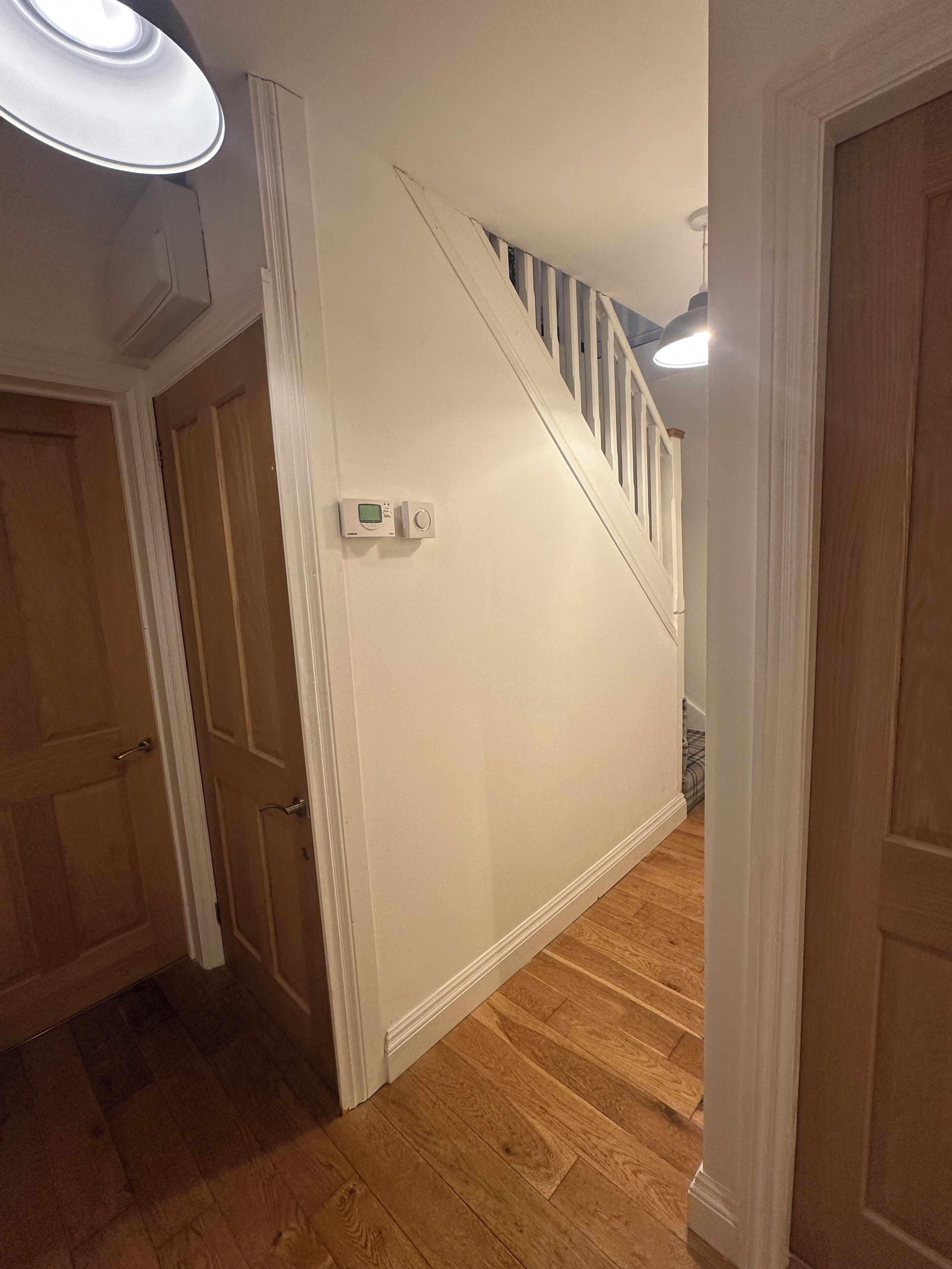 Un pasillo con piso de madera, pared blanca y una escalera con barandillas blancas.