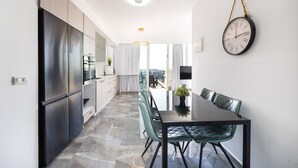 A modern kitchen with a dining area, a hanging clock, and a view to the outside. - Premium and Luxe 2BR by the Shuk – Free Parking (Jerusalem)