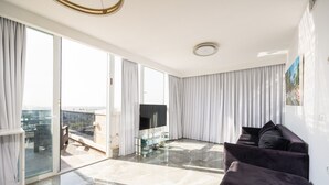 A spacious living room with a large flat-screen TV, a dark-colored sofa, and a glass coffee table. - Premium and Luxe 2BR by the Shuk – Free Parking (Jerusalem)