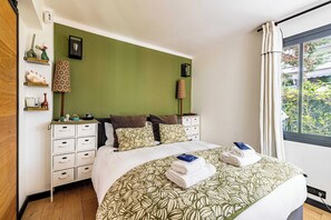 A neatly made bed with a patterned bedspread, a bedside table with a lamp, and a window with curtains. - Charming Apartment With Terrace a/c 4P - Cannes (Cannes)