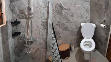 A bathroom with a shower, toilet, and marble walls.