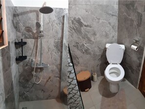 A bathroom with a shower, toilet, and marble walls.