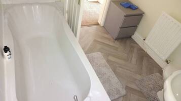 A bathroom with a bathtub, toilet, and a small cabinet.