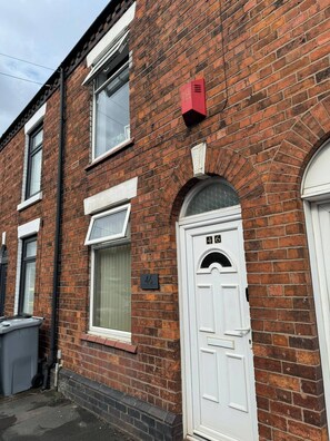 Una casa de ladrillo rojo con una puerta blanca, una ventana y una placa con un número.