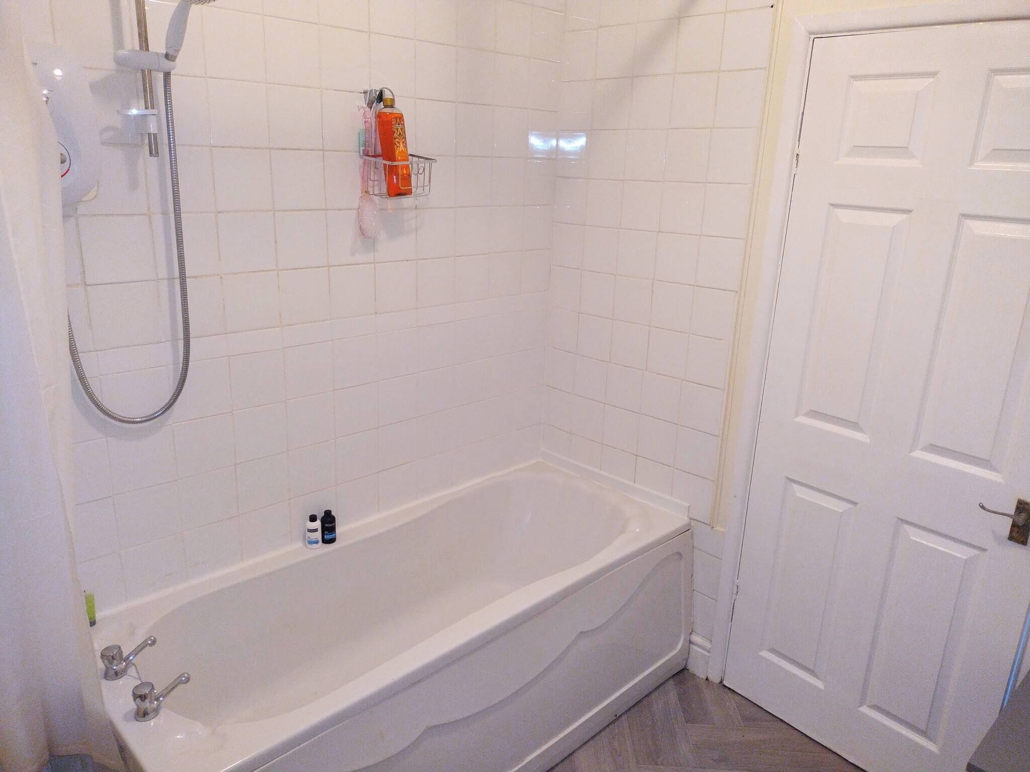 A bathroom with a white bathtub, a shower, and a door.