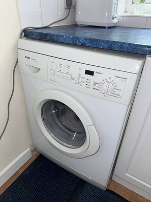 A Bosch EXCEL 1100 Express front-loading washing machine with a control panel, a blue countertop above, and a wooden floor. - Bentley View,2 bed House Crewe (Crewe)