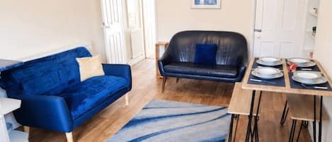 Un espacio habitable compacto con un sofá azul, un sofá de cuero negro, una mesa de comedor con sillas y una alfombra azul.