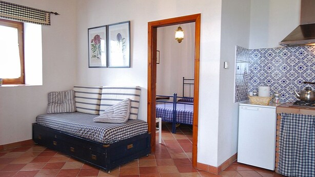 A compact room with a bed, a kitchenette, and a door leading to another room. - Villa Opera - Apartment in Livorno (Toscana)