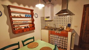 A kitchen with a wooden shelf, a table with a checkered tablecloth, and a tiled backsplash. - Villa Opera - Apartment in Livorno (Toscana)