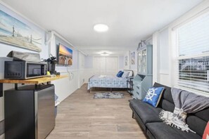 Ein gemütlicher Raum mit Küchenzeile, einem Bett, einer Couch und einem Fenster mit Jalousien.