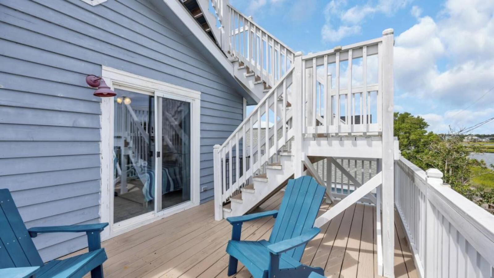 Une terrasse en bois avec un escalier menant à un espace abrité, deux chaises et une vue sur une étendue d’eau.