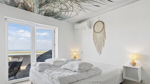 Une chambre avec un lit, un attrape-rêves, une table de chevet et une vue sur la plage.