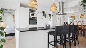 Une cuisine moderne dotée d’un îlot central, de luminaires suspendus et d’une hotte de cuisine en acier inoxydable.