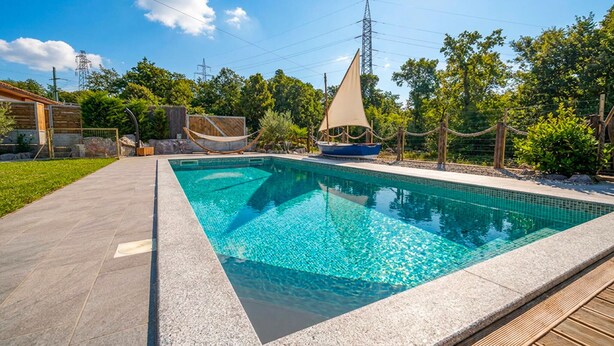 Ein Swimmingpool mit einer Segelboot-Dekoration, umgeben von einer Holzterrasse und einer Rasenfläche.