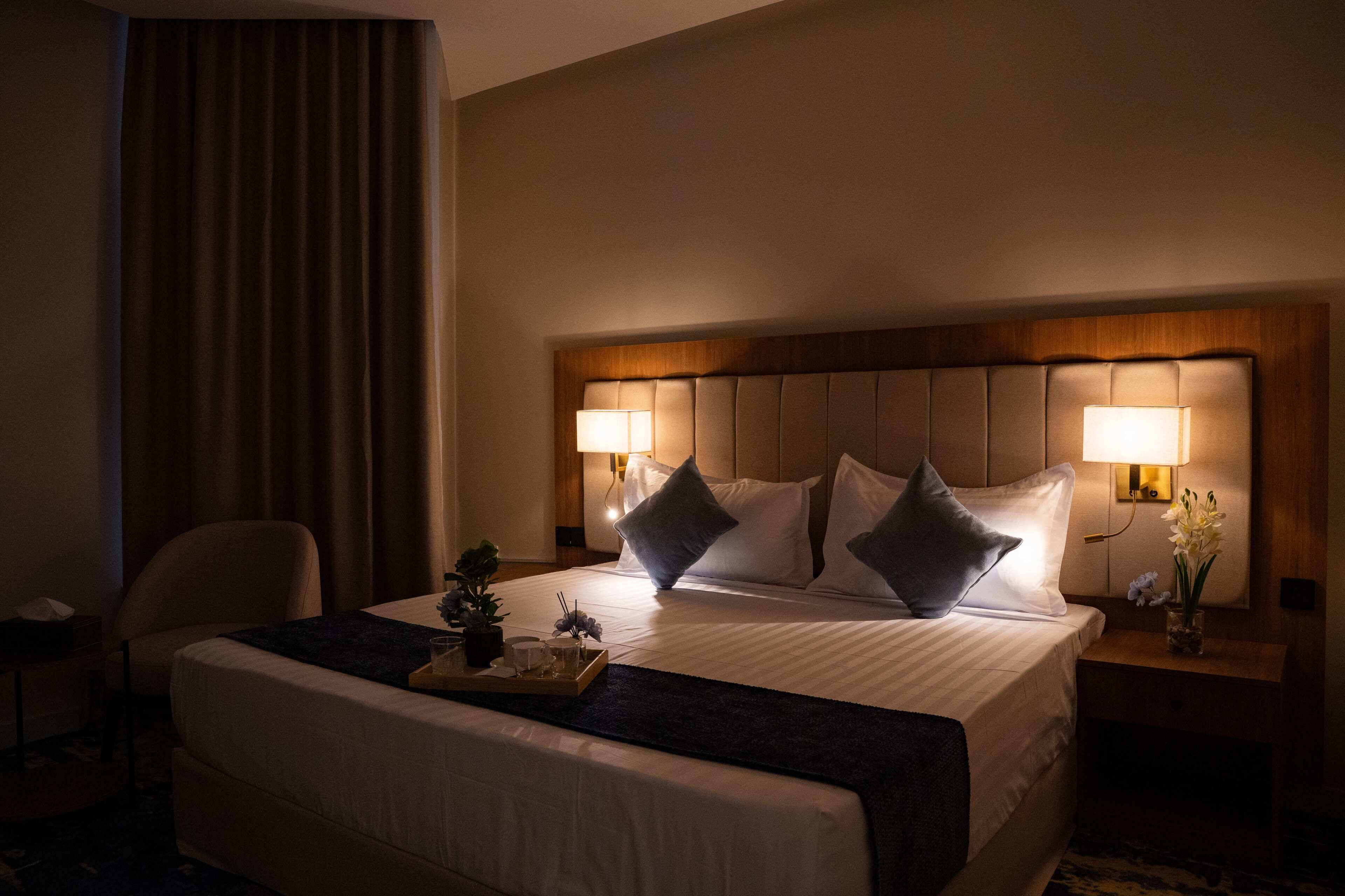 A hotel room with a large bed, two bedside lamps, a nightstand with a vase of flowers, and a chair.
