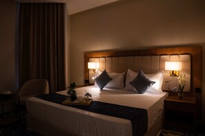 A hotel room with a large bed, two bedside lamps, a nightstand with a vase of flowers, and a chair. - H SAM HOTEL (Taif)