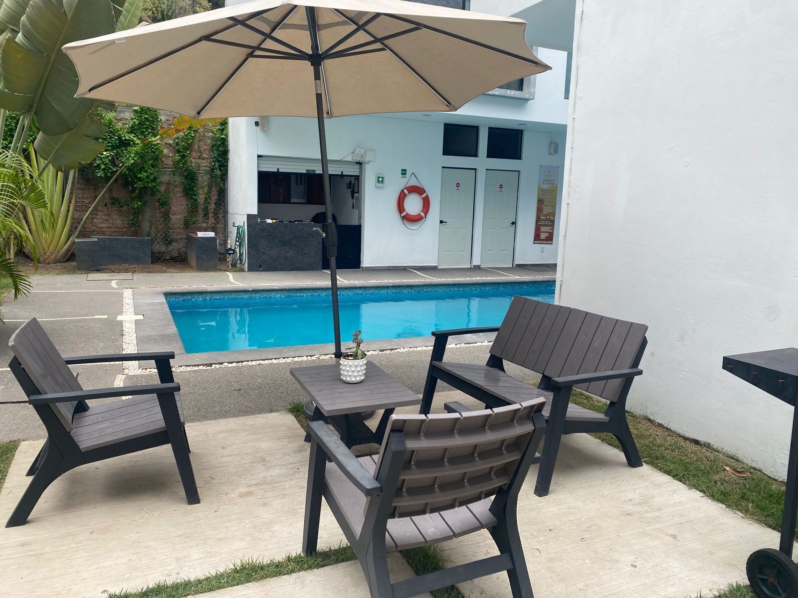 Zona de piscina con dos sillas, una mesa, una pileta y un edificio con un flotador salvavidas.