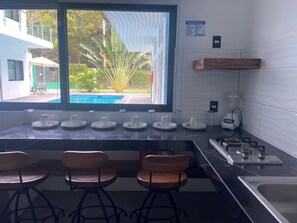 Una cocina con un ventanal grande, una estufa a gas y tres taburetes de bar.