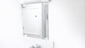 Ein Badezimmer mit weiß gefliesten Wänden, einer weißen Toilette und einem weißen Waschbecken mit Wasserhahn.