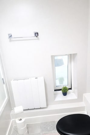 A bathroom with a toilet, a radiator, a towel rack, a window with a plant, and a roll of toilet paper. - Stylish Duplex in the Heart of Walsall (Walsall)