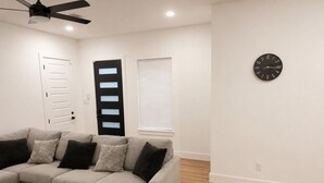 A living room with a sectional sofa, a ceiling fan, a clock on the wall, and a door with frosted glass panels. - Delightful 3-bedroom house with AC in vibrant Houston (Houston)
